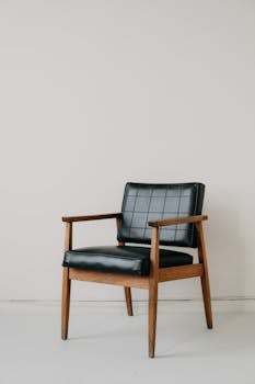 Classic mid-century modern armchair with black leather upholstery on minimalist backdrop, capturing retro style.
