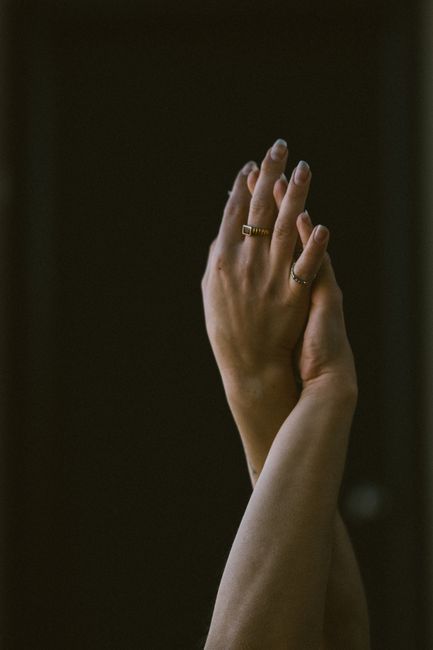 Graceful hands adorned with rings against a dark background, showcasing elegance and style.