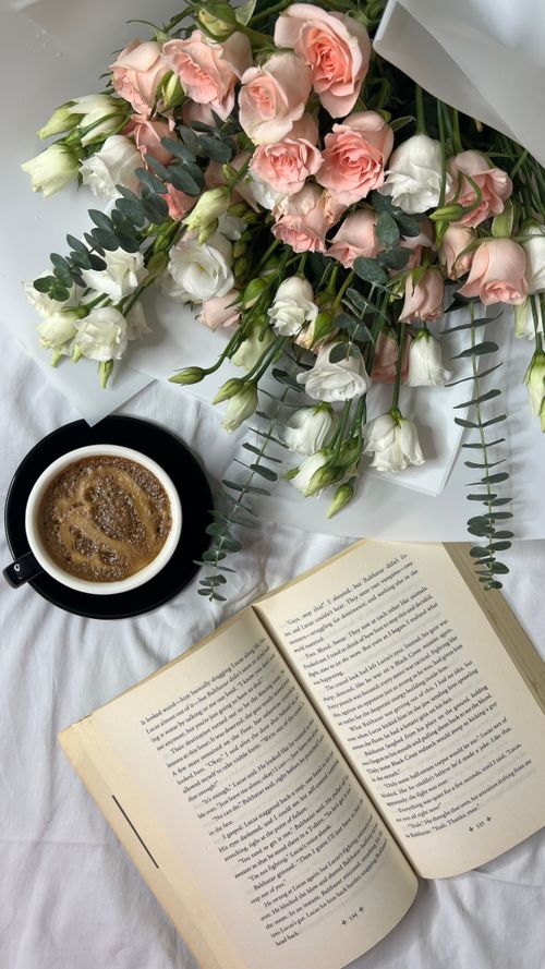 Free A peaceful morning setup featuring fresh roses, a steaming cup of coffee, and an open book. Stock Photo