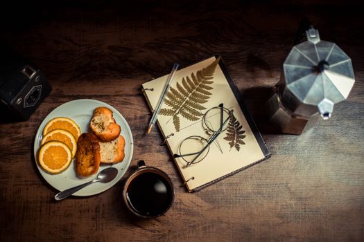 A warm breakfast setup with coffee, orange slices, and a notebook.