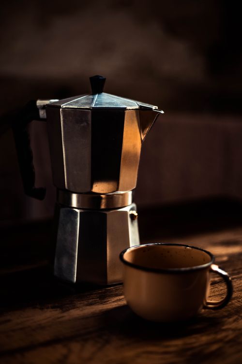 Free Close-up of a moka pot with a coffee cup on a wooden table, in warm lighting. Stock Photo