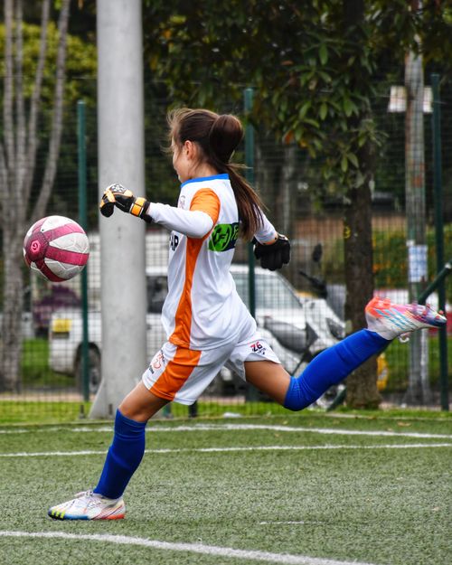 Free A young female soccer player actively kicking a ball during a game on a grass field. Stock Photo