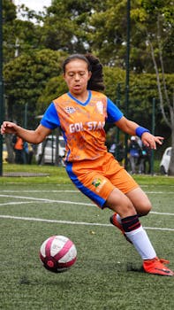 Young woman playing soccer outdoors in vibrant sportswear, showcasing dynamic action.