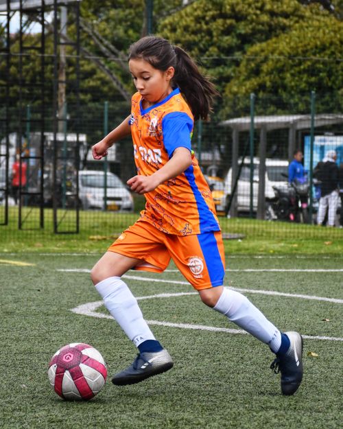 Free Teenage girl in sports clothing kicking a football on an outdoor field. Stock Photo