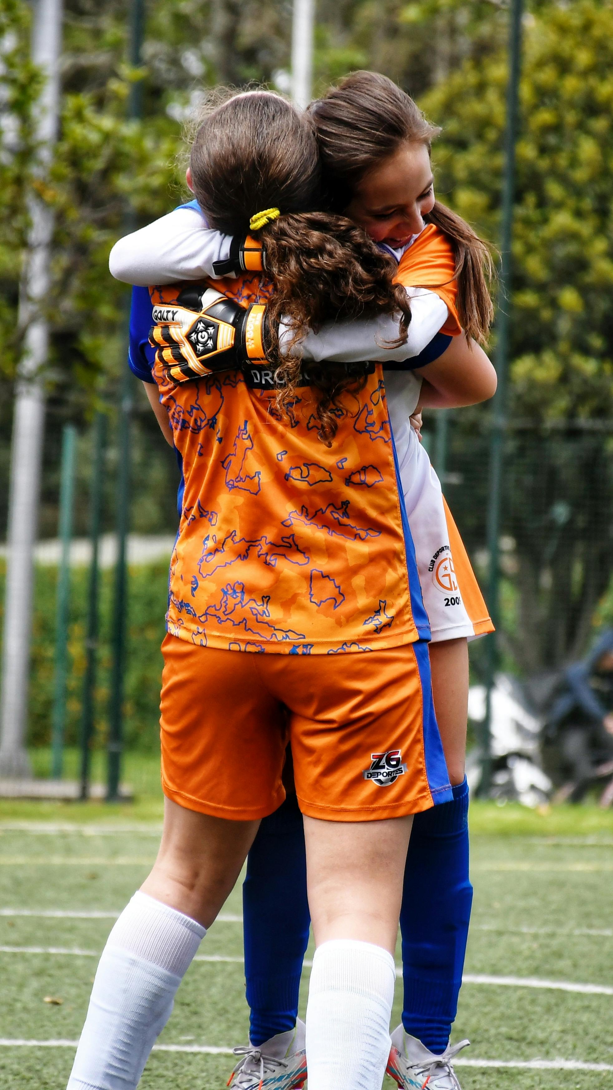 Two young soccer players embracing in celebration on a sunny day.