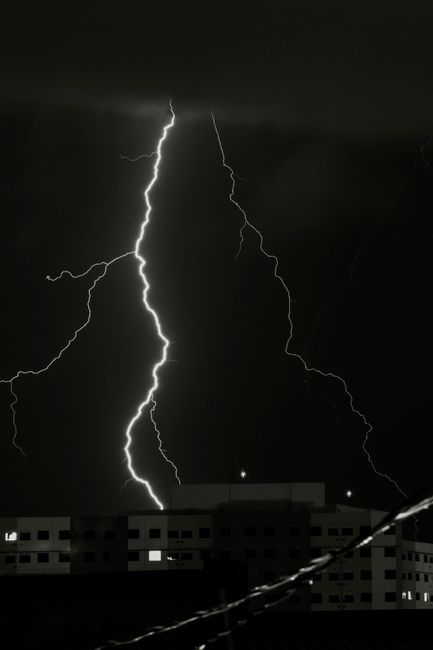 A striking lightning bolt illuminates the sky above buildings during a stormy night.