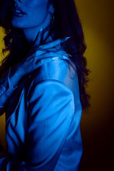 Stylish woman in silk blouse posing with dramatic blue and yellow lighting.