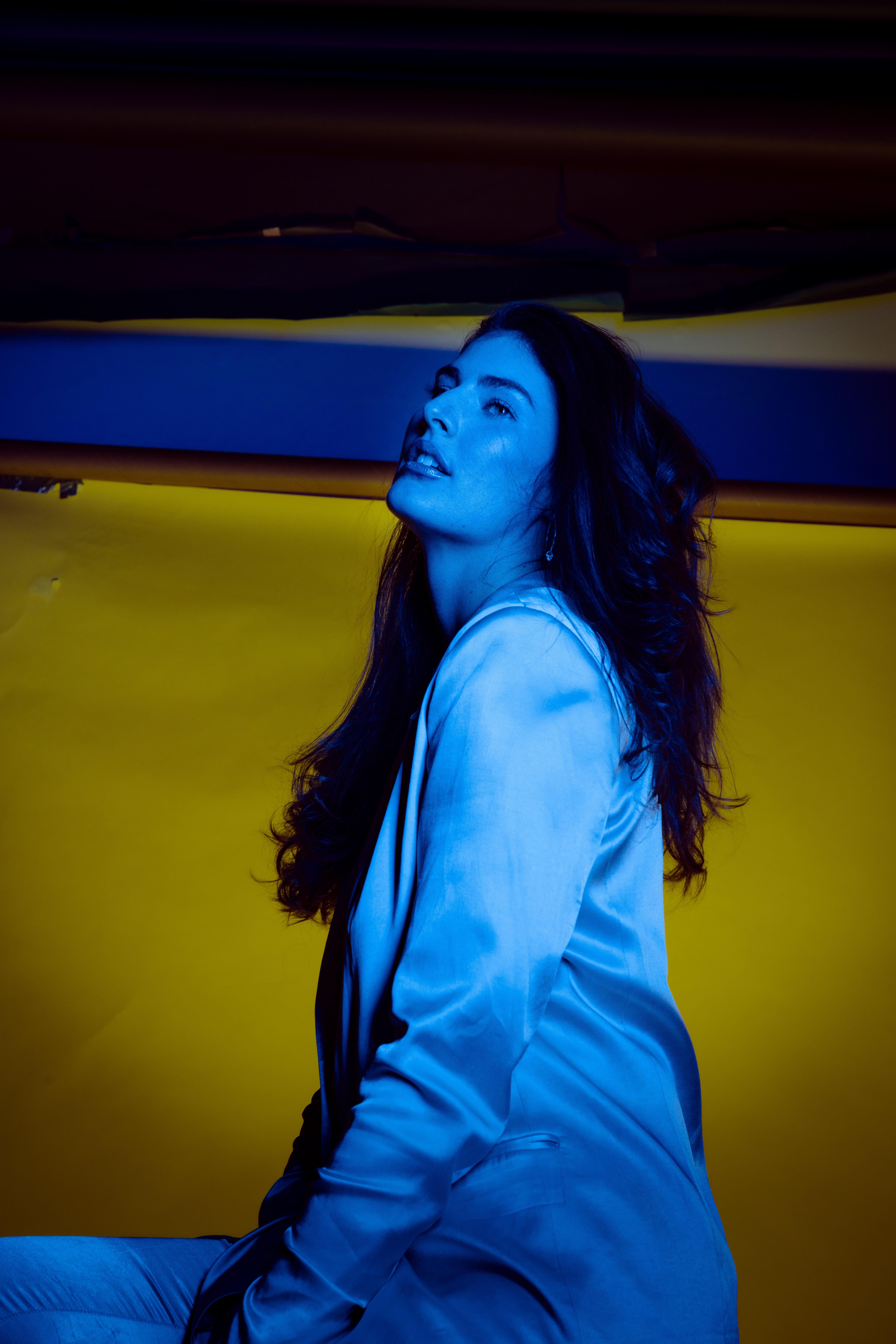 Captivating portrait of a brunette woman in blue light with a yellow background.