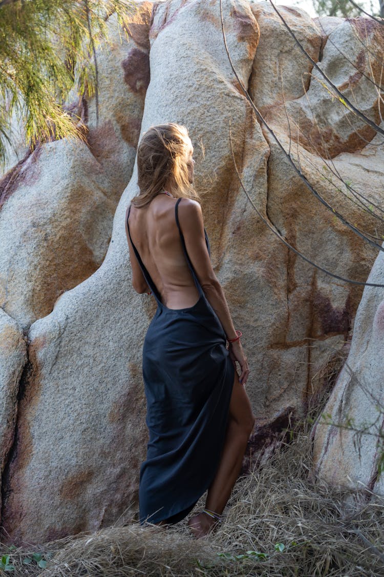 Woman In A Backless Dress Standing Near Rock