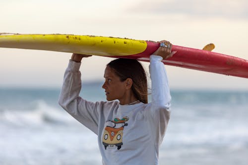 A Woman in a White Sweatshirt Carrying a Surfboard