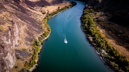 Free Aerial shot of a speedboat gliding on a winding river with rocky cliffs and lush greenery. Stock Photo