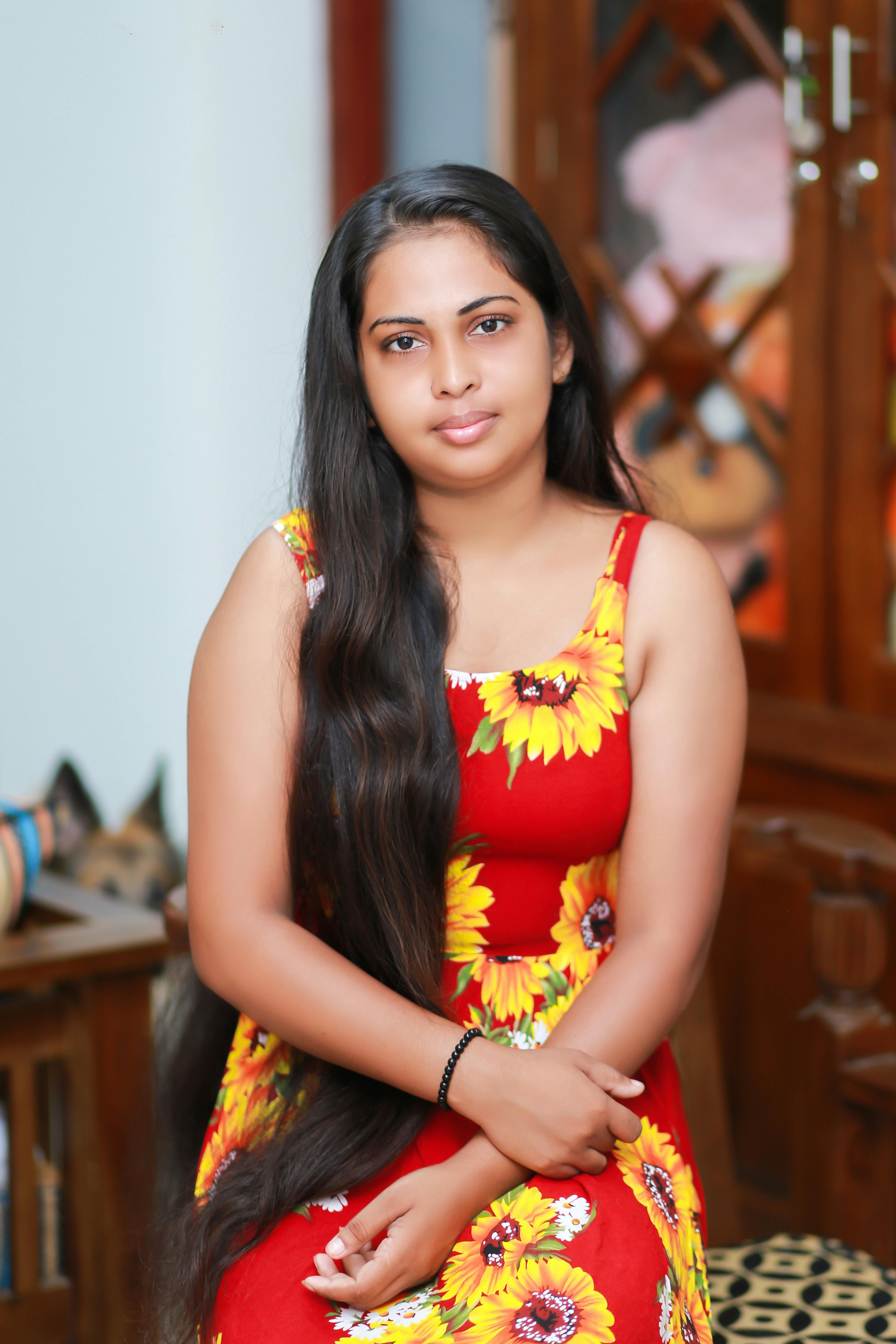 Free Portrait of a young woman with long hair in a vibrant floral dress, sitting indoors. Stock Photo