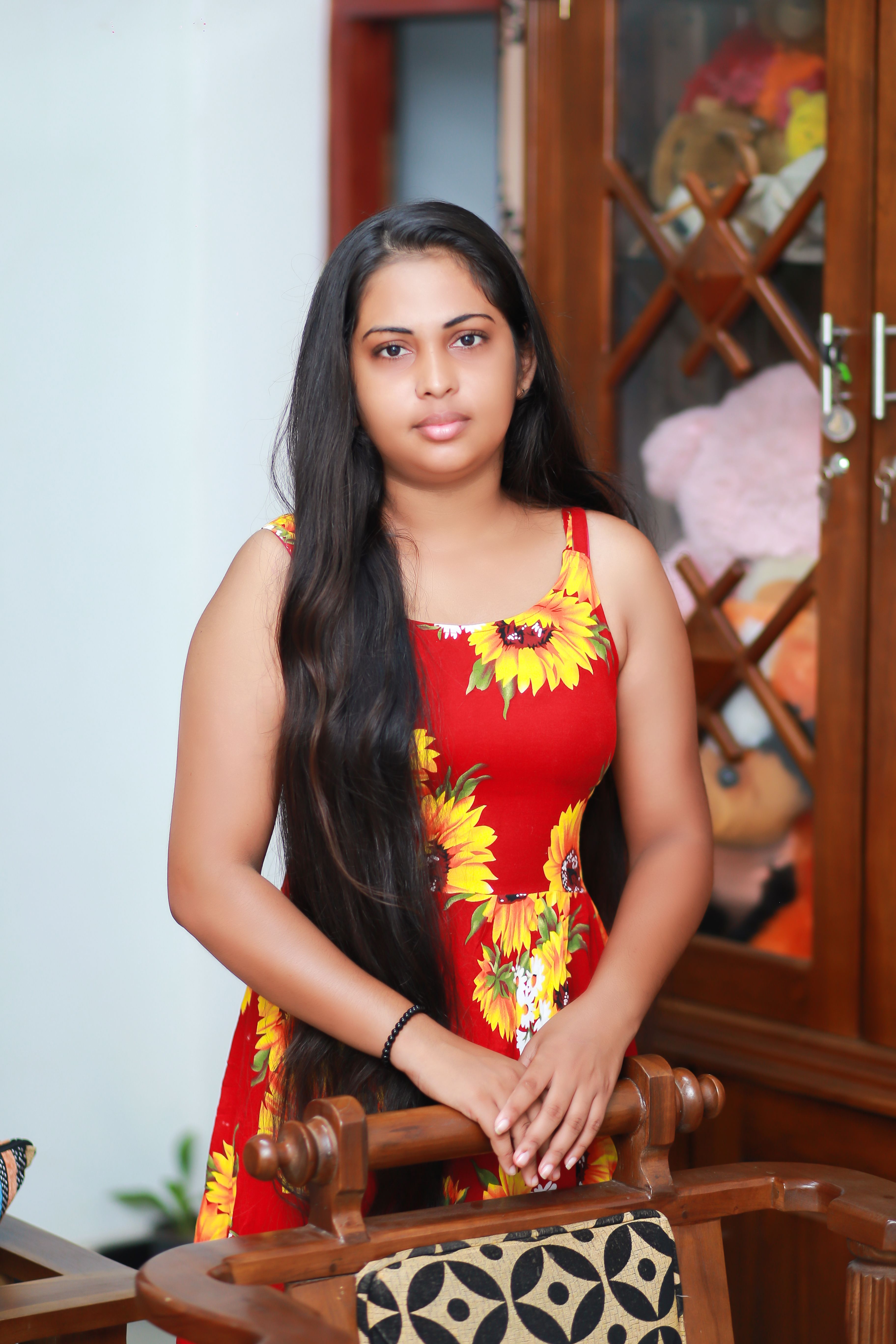 Portrait of a young woman in a floral dress posing indoors with a wooden furniture backdrop.