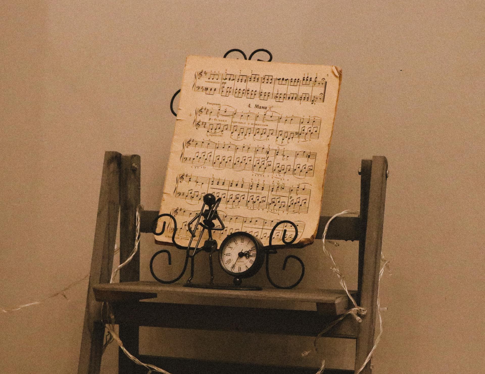 An artistic setup of a vintage music sheet with a clock and figurine on a wooden stand.