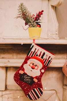 A colorful Santa-themed Christmas stocking hanging by the fireplace, with decorative plants above.