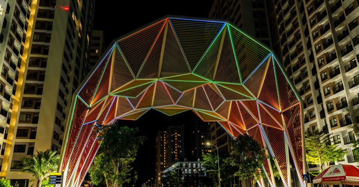 Vibrant geometric arch with colorful lights amidst urban high-rise buildings at night.