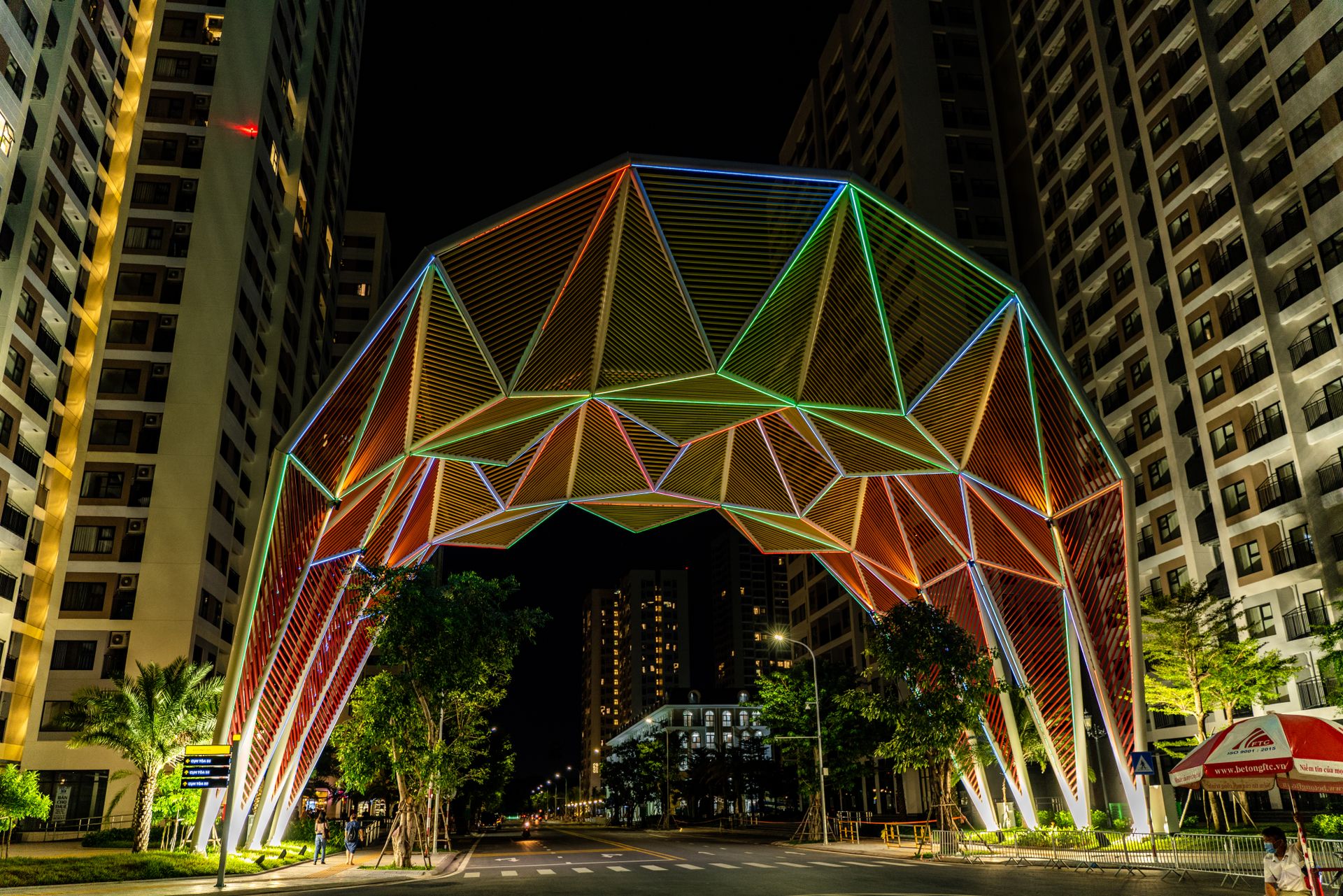 Vibrant geometric arch with colorful lights amidst urban high-rise buildings at night.