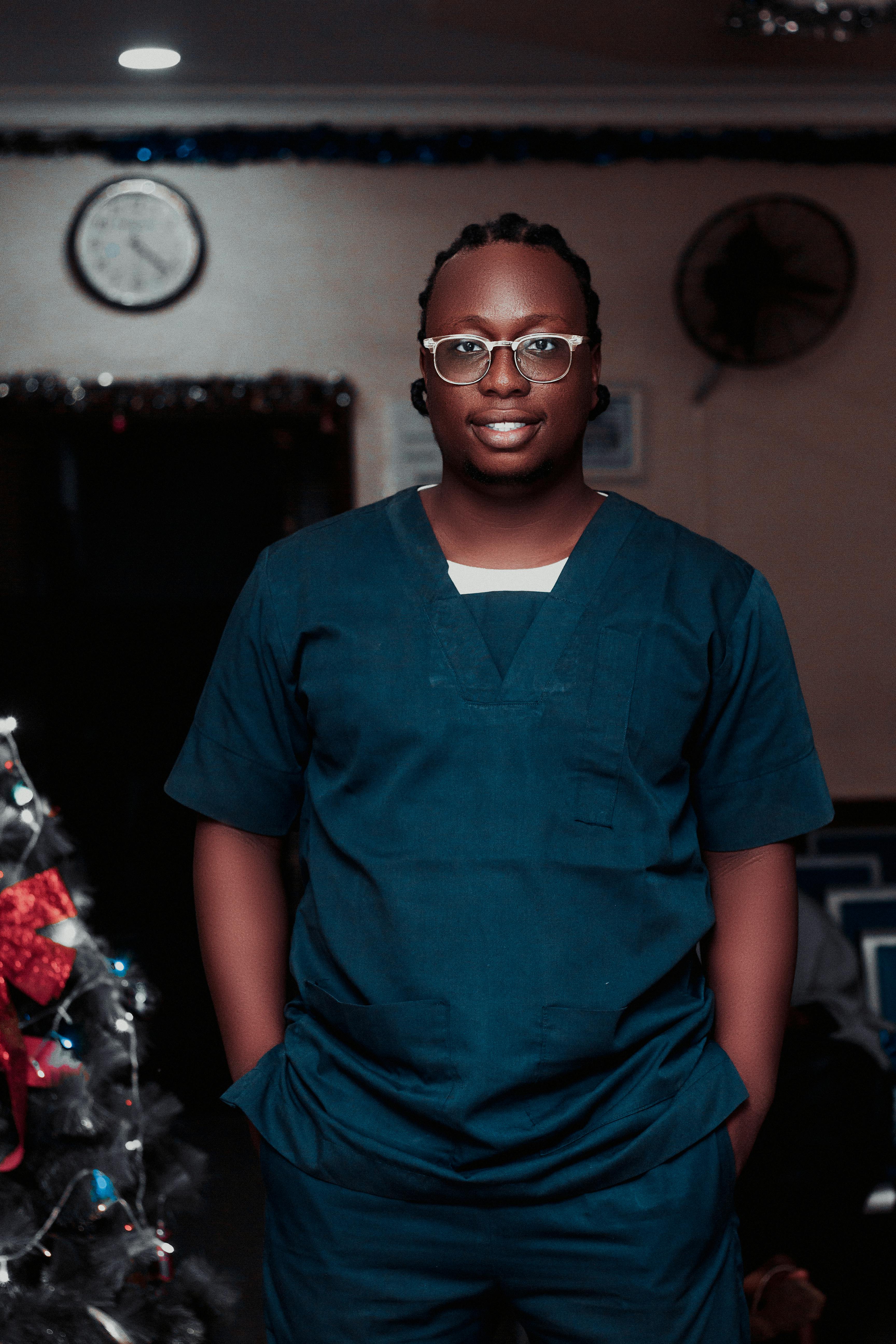 A smiling healthcare worker in scrubs by a festive Christmas tree, embodying holiday cheer.