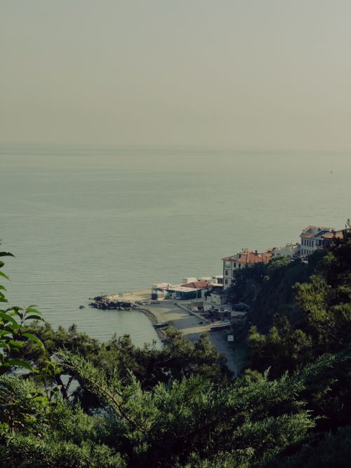 Free A serene coastal scene with buildings nestled by the tranquil sea, surrounded by lush greenery. Stock Photo