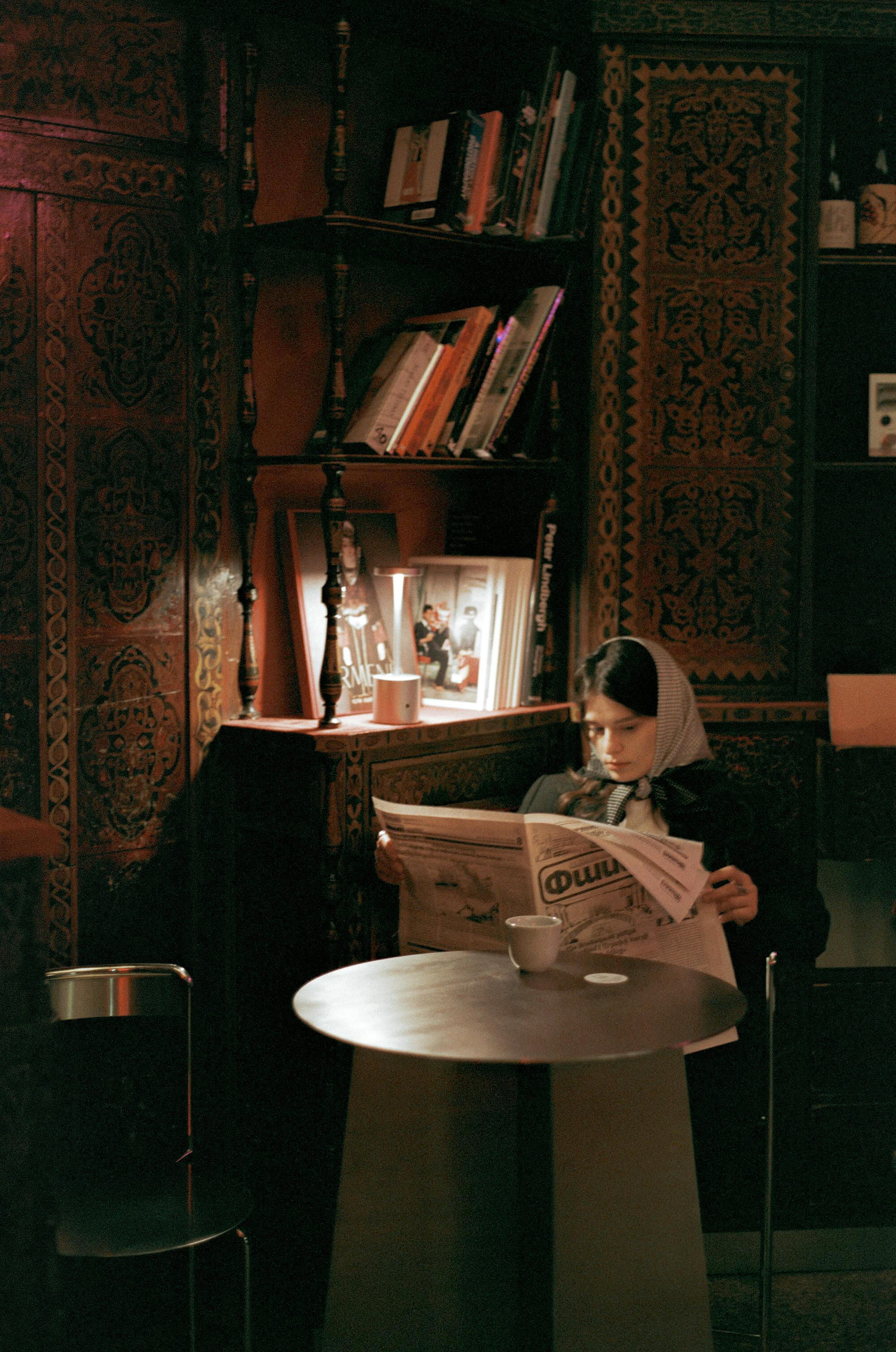 Young woman reads a newspaper in a charming Yerevan café, surrounded by warm, cozy decor.