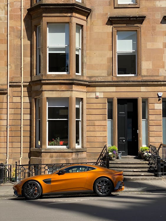 Free Orange luxury sports car parked in front of a classic Glasgow townhouse. Stock Photo