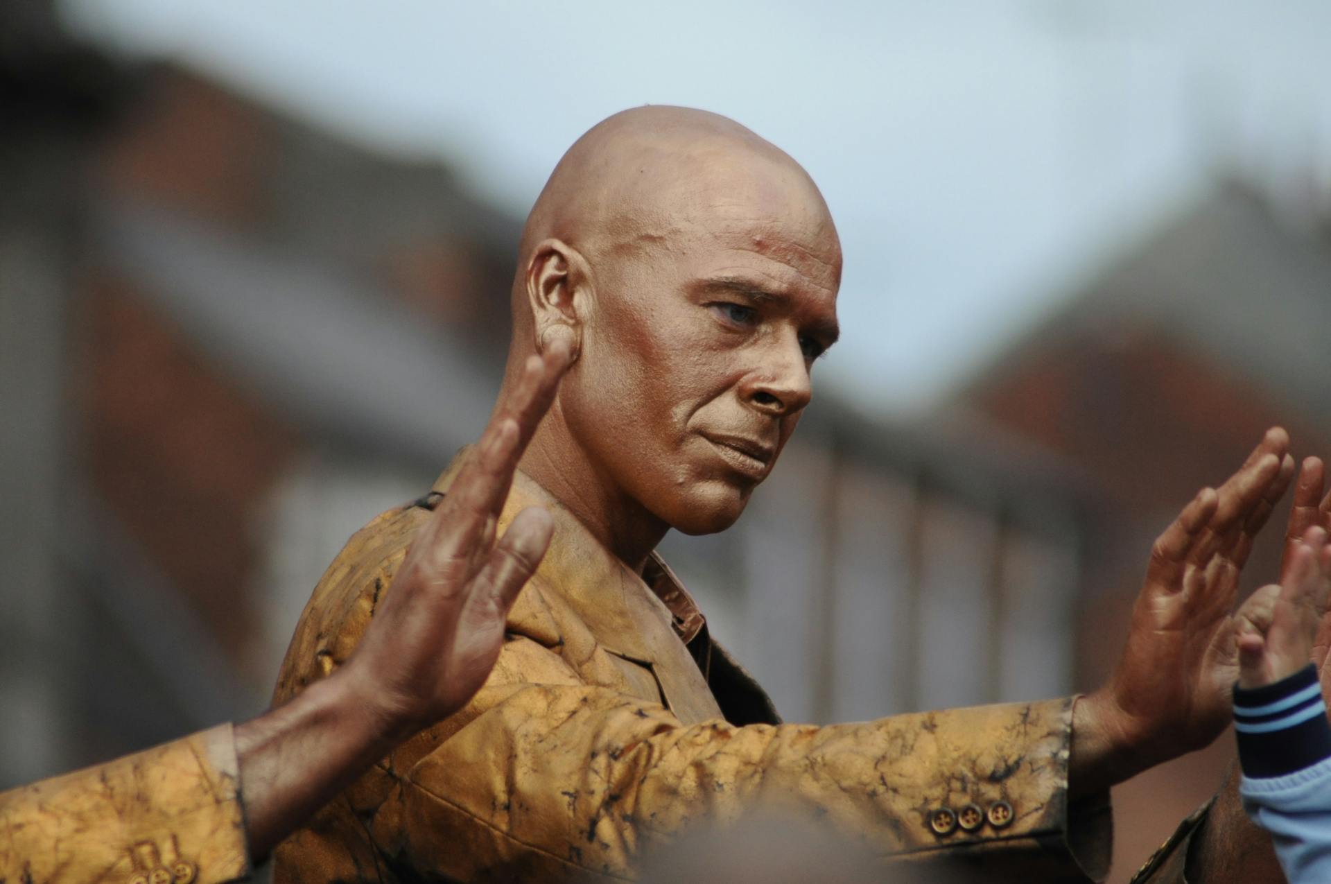 Street performer painted in gold gives a high five outdoors. Unique cultural expression captured.