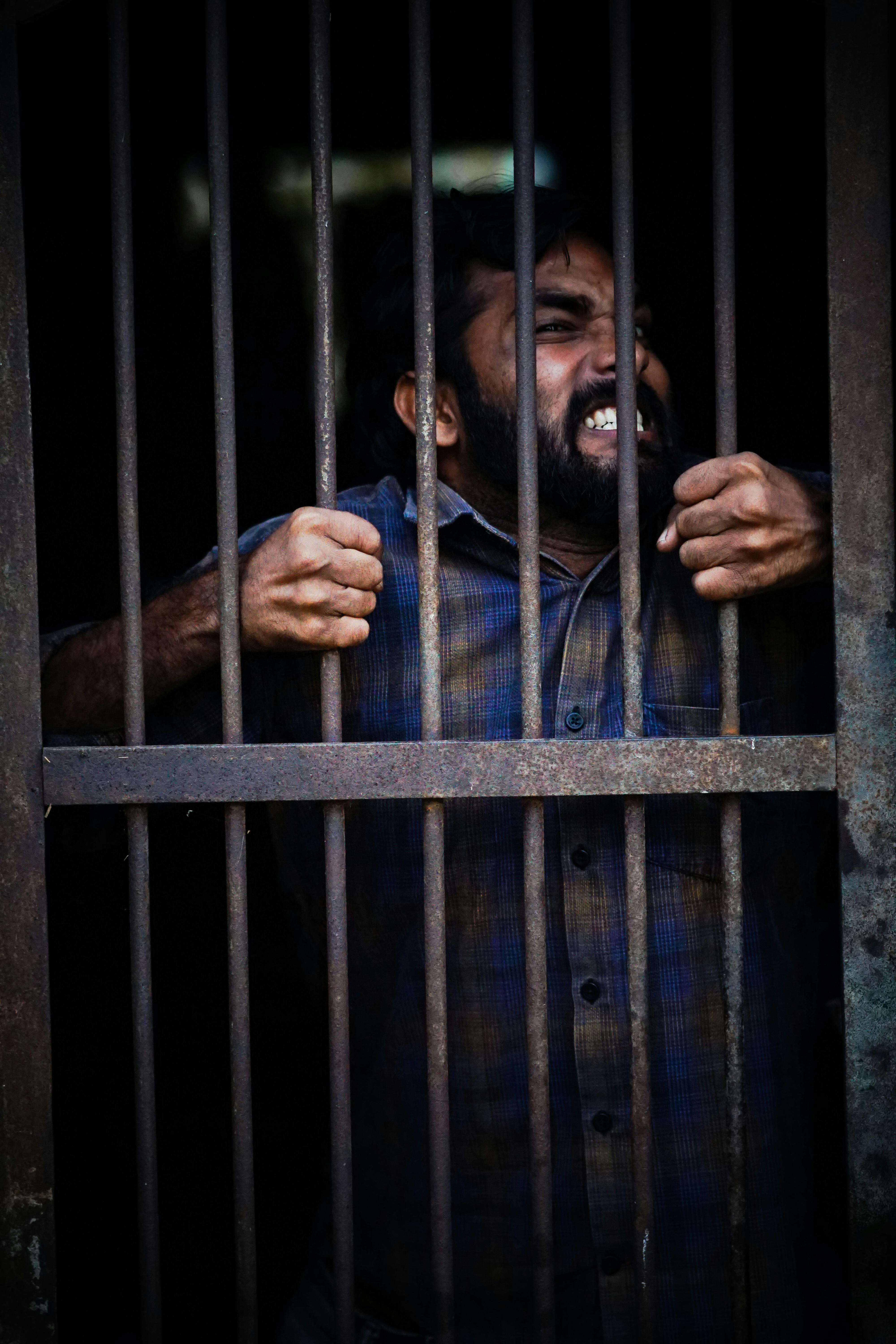 a man wearing a blue plaid shirt behind grey bars