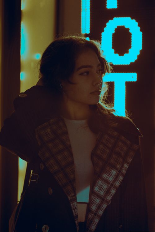 Free Woman posing with hand in hair under bright neon lights, exuding fashion and style. Stock Photo