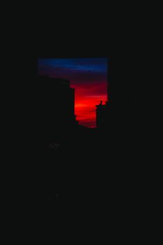 Silhouette of city buildings at sunset with vibrant red and blue sky.