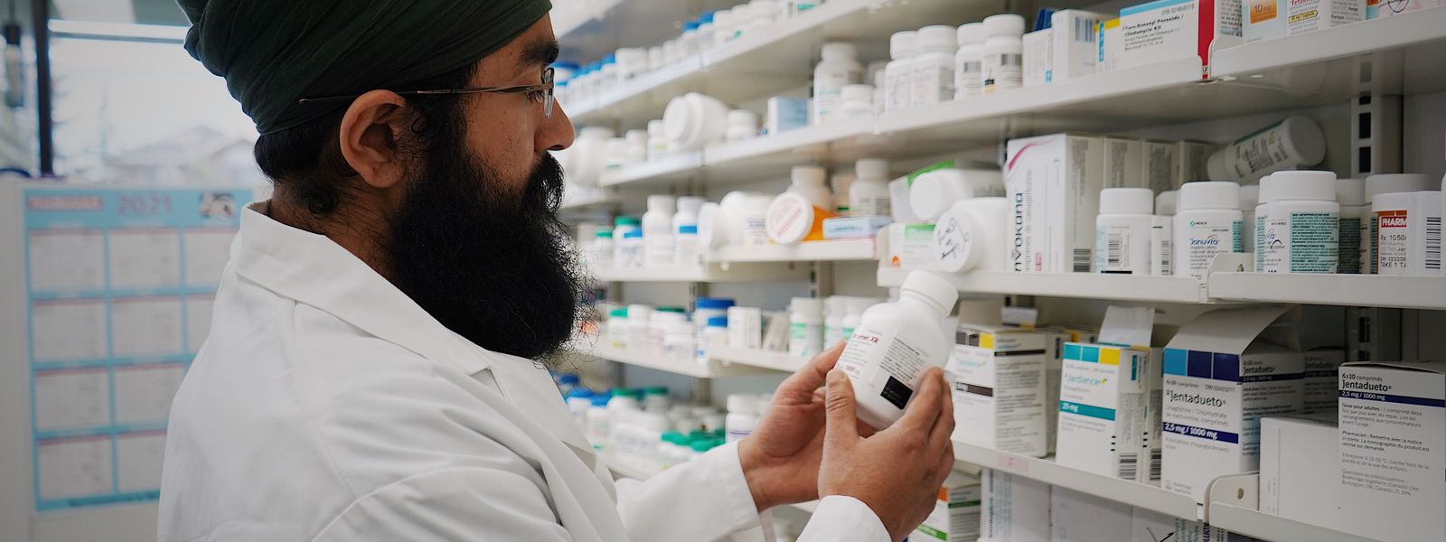 Pharmacist with turban organizing shelves in a pharmacy, focused on healthcare.
