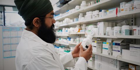 Pharmacist with turban organizing shelves in a pharmacy, focused on healthcare.