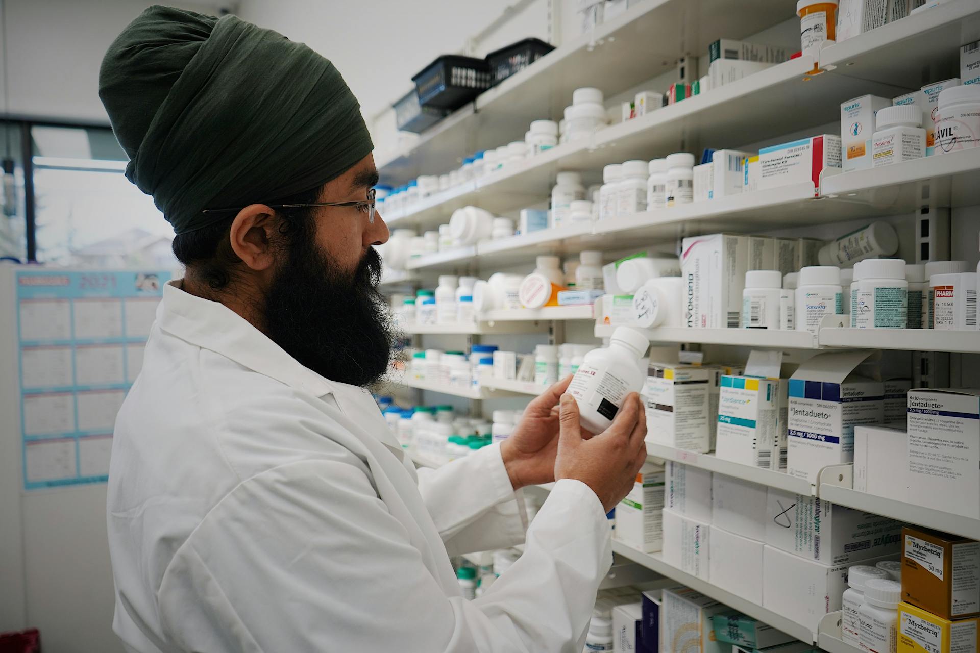 Pharmacist with turban organizing shelves in a pharmacy, focused on healthcare.