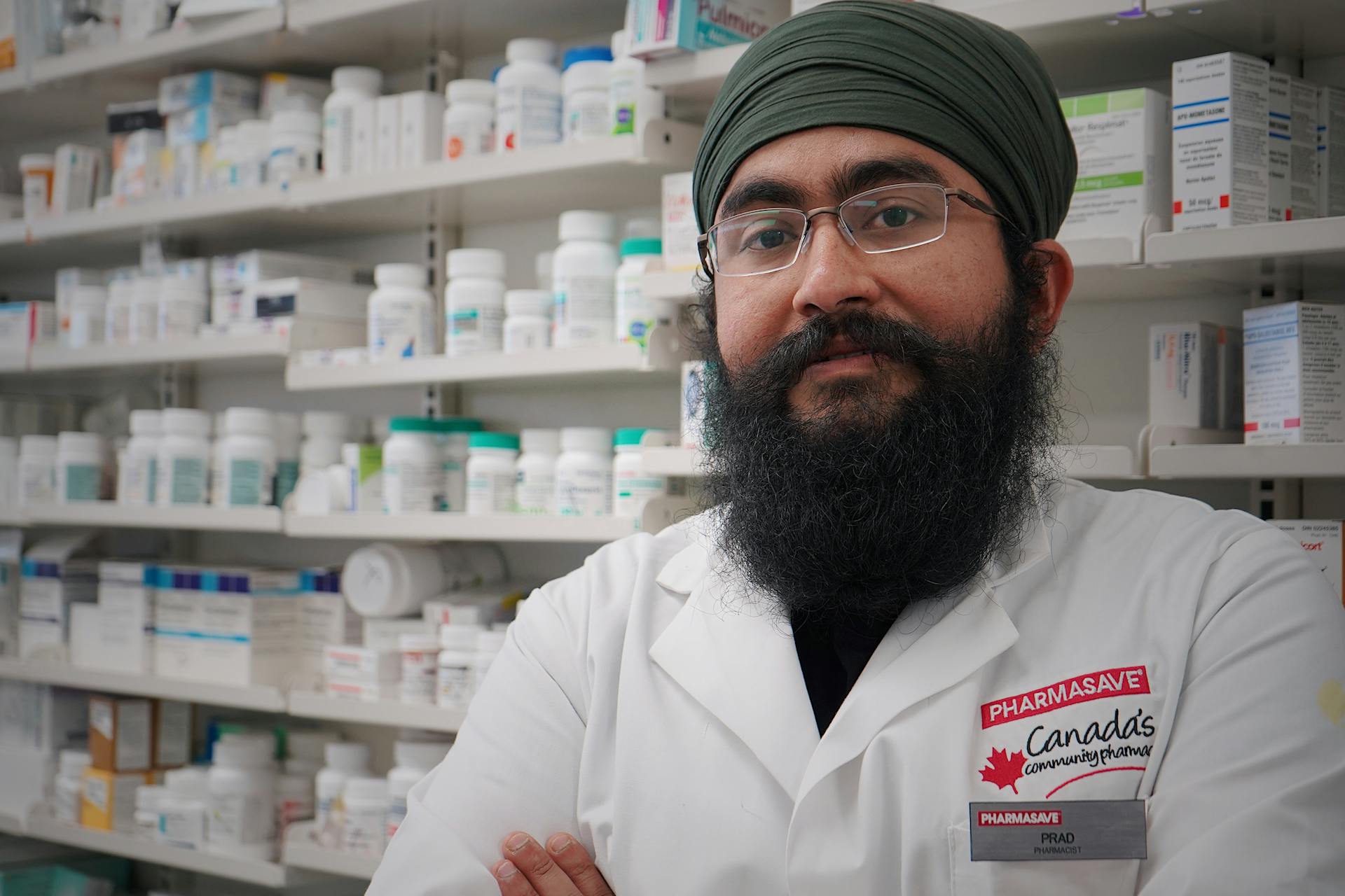 A professional pharmacist with a turban and beard stands confidently in a pharmacy aisle.