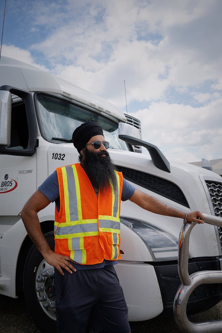 A Man Wearing A Black Head Turban And Orange Safety Vest Standing Beside A Truck 