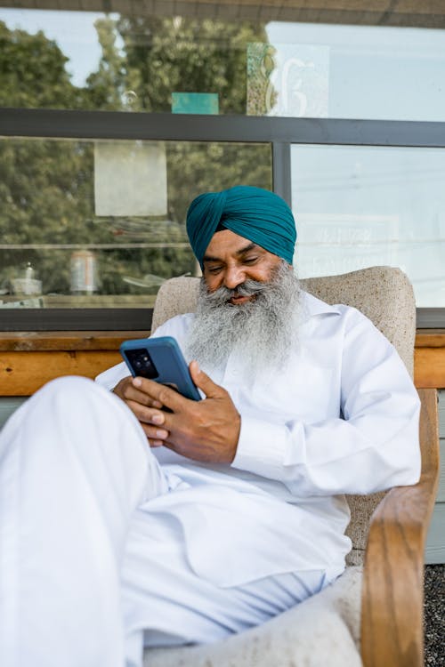 Man in Turban Looking at Cellphone and Smiling
