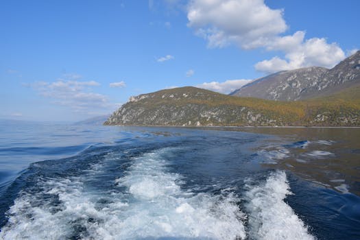 Capture the serene beauty of Ohrid's lake against a backdrop of rugged mountains and clear skies.