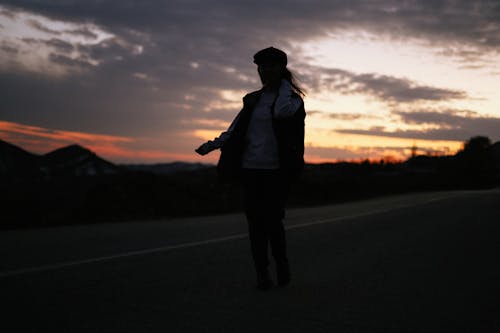 Silhouette of a Woman Walking on a Road at Sunset