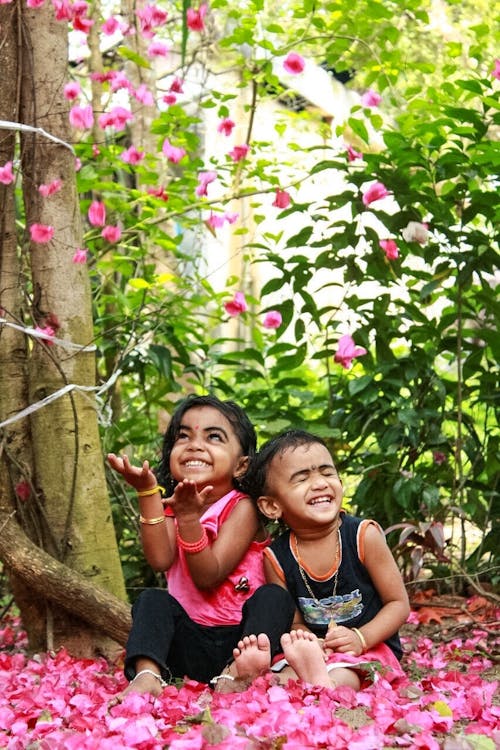 Free Laughing Boy and Girl Sitting on Pink Flower Petals Near Tree Stock Photo