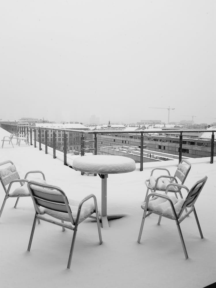 A Table And Chairs On A Balcony Covered In Snow 