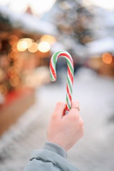 A festive candy cane held up against a blurred winter market backdrop, evoking holiday joy.