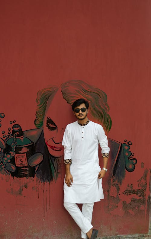 A Man in White Sherwani Wearing Sunglasses while Leaning on the Wall