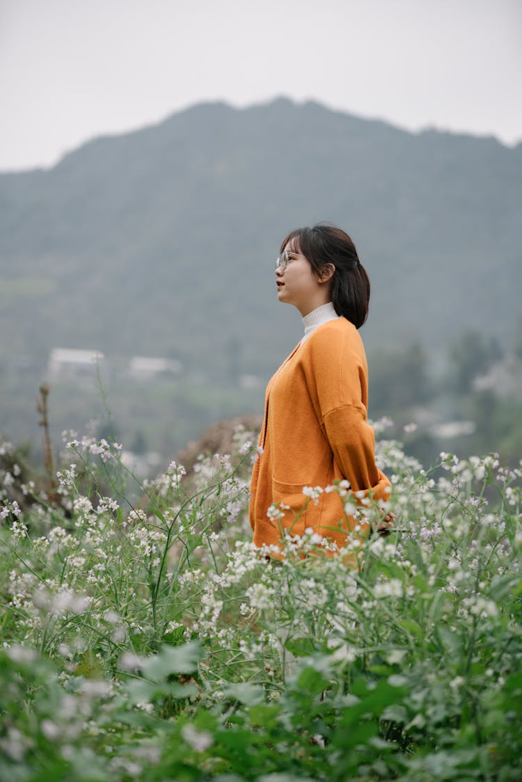 A Woman In Brown Cardigan Standing On White Flower Field While Looking Afar