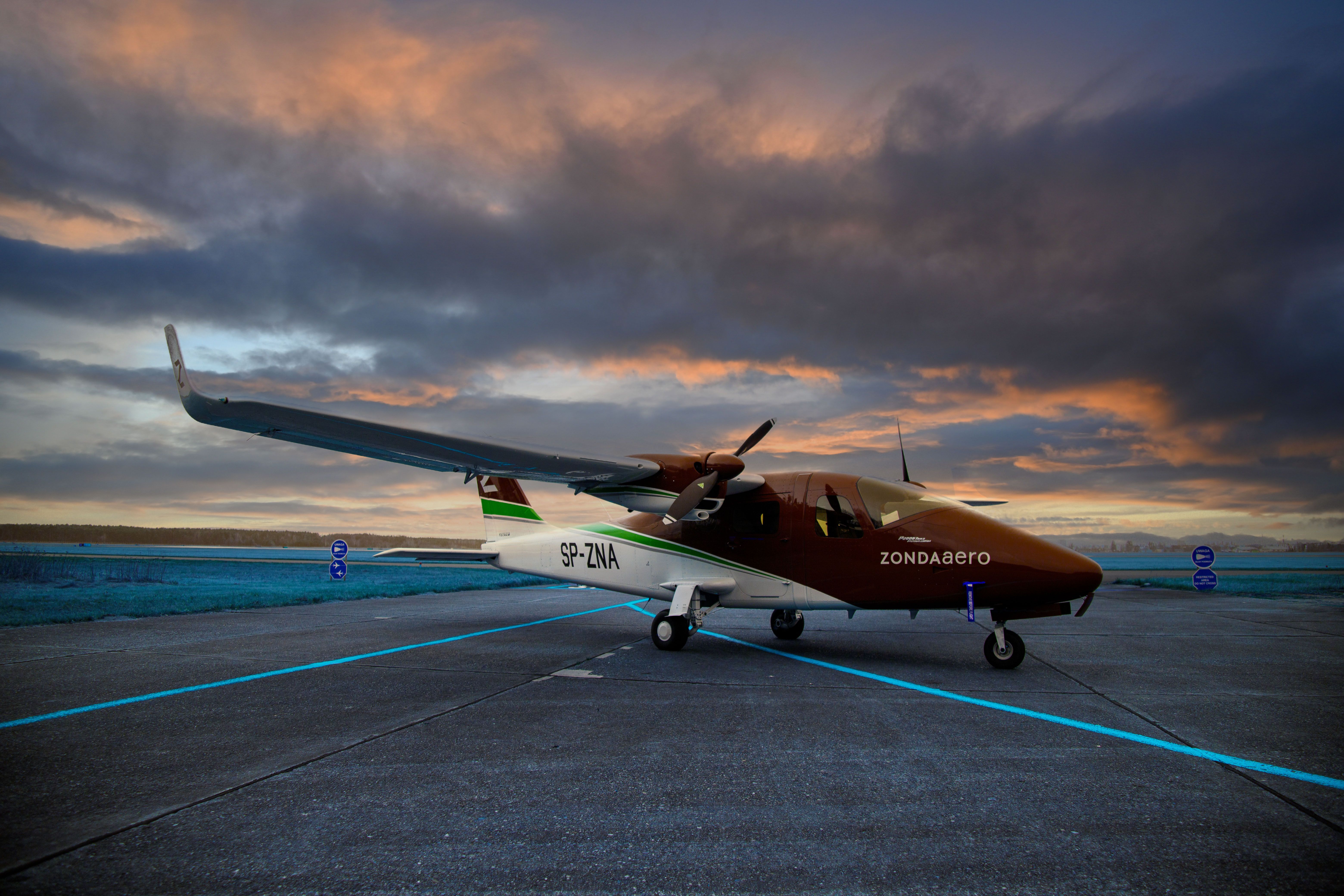 A scenic view of a light aircraft parked on the tarmac during a vibrant sunset.