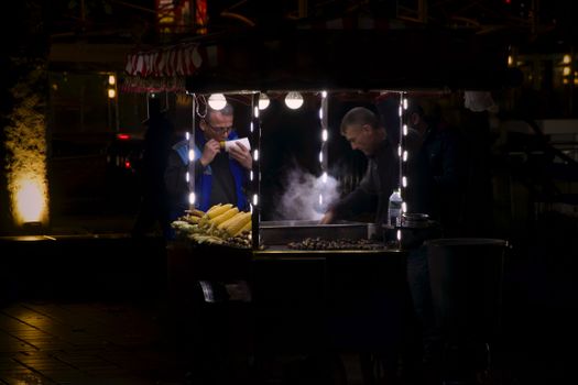 Street vendor sells roasted corn under bright lights at night, showcasing a culinary experience.