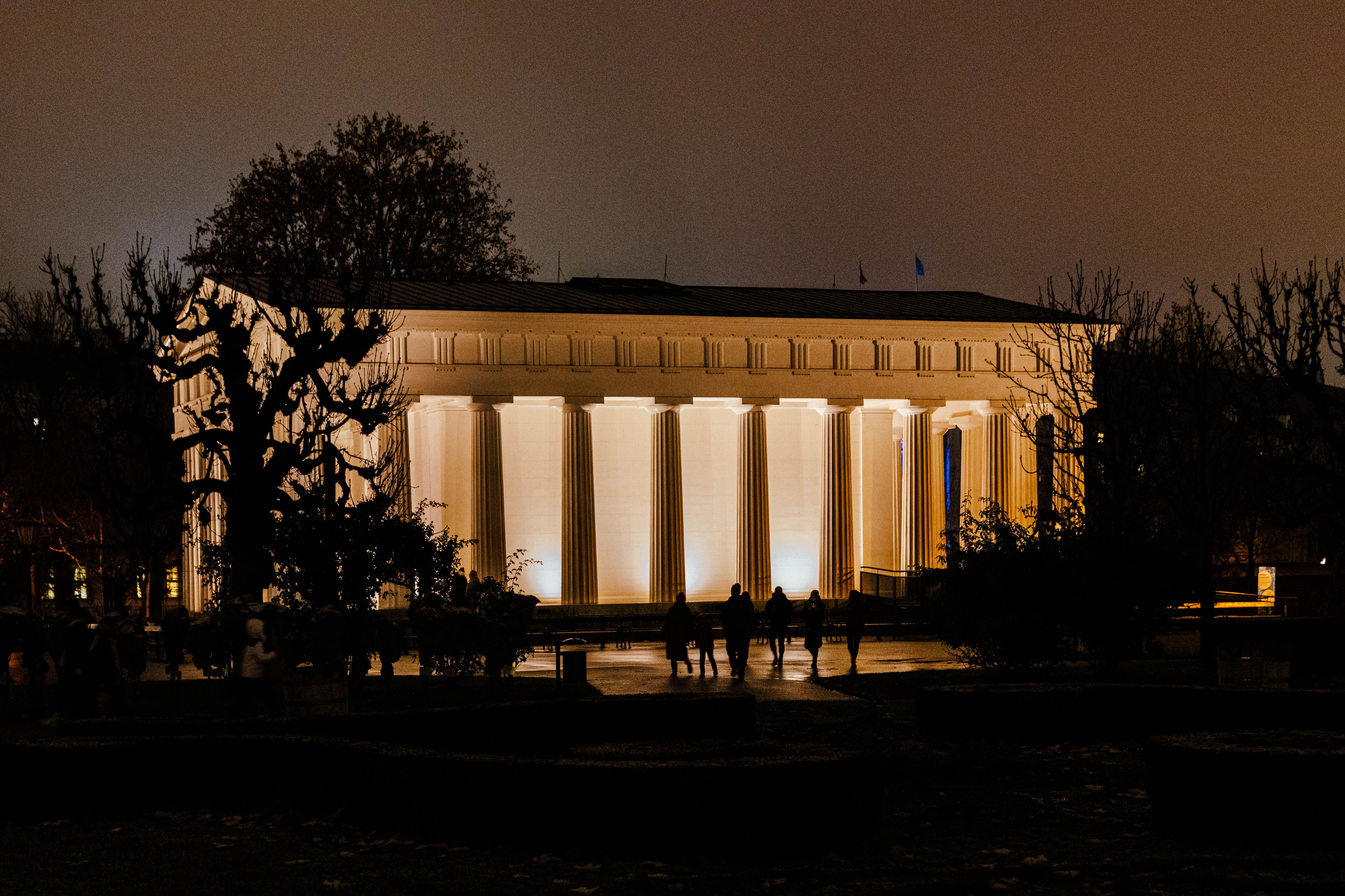 Illuminated neoclassical temple in Volksgarten, Vienna at night with silhouetted visitors.
