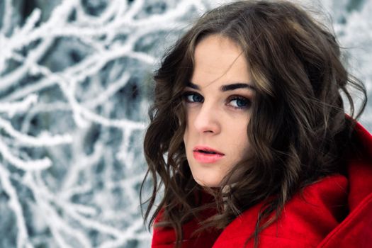 Captivating winter portrait of a woman in a red coat with frosty background.