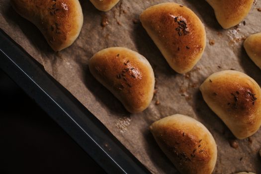 A batch of golden, freshly baked bread rolls with herbs on parchment paper.