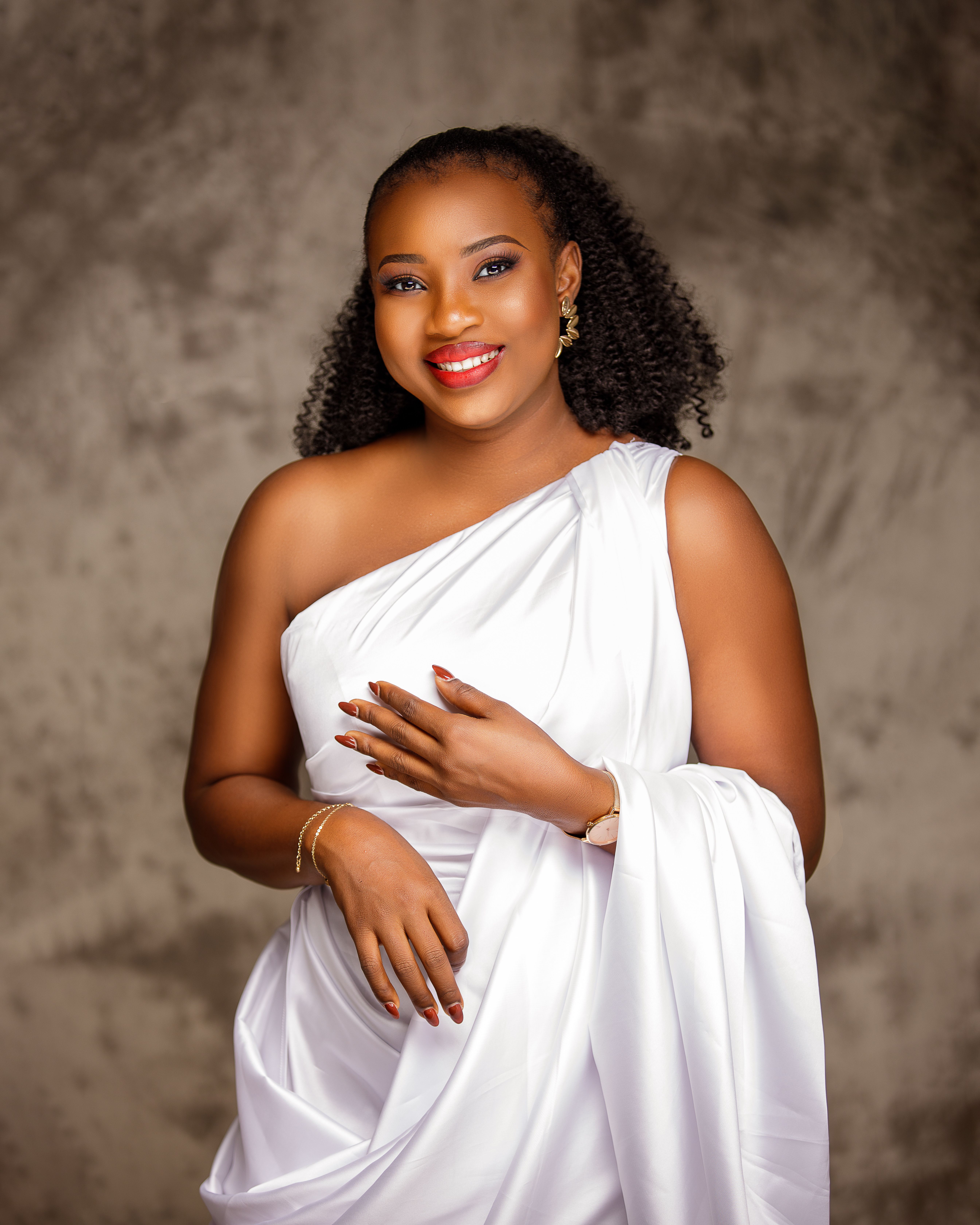 Portrait of a smiling woman in a stylish white dress posing elegantly indoors.