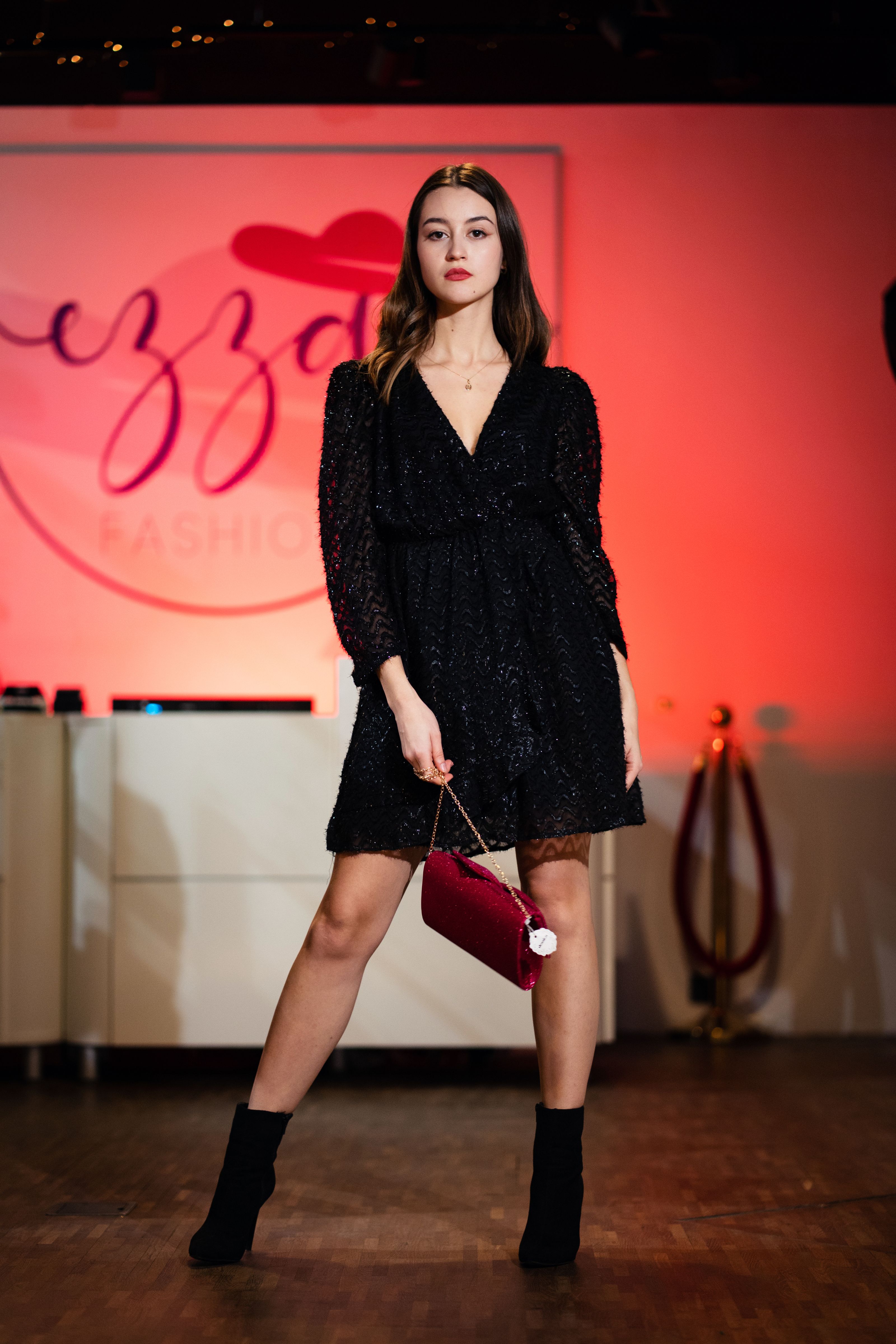 Modelo de moda posando em um vestido preto brilhante com bolsa vermelha na pista.
