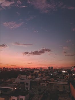 A beautiful sunset casting warm hues over a bustling urban landscape with rooftops and distant skyscrapers.